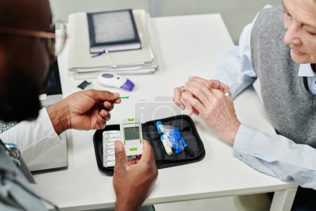 Photo for Hands of young African American doctor showing mature patient glucometer before medical test of sugar level in blood - Royalty Free Image