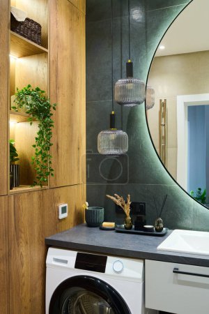 Téléchargez les photos : Corner of spacious bathroom with washing machine, mirror, closet and self love items standing on tray with two lamps hanging above - en image libre de droit