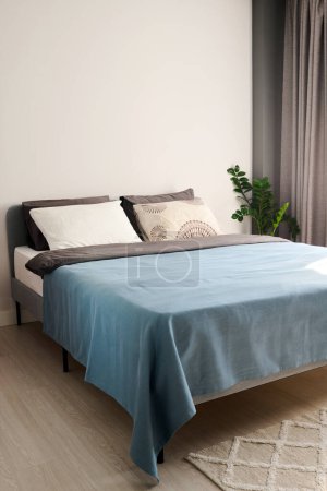 Téléchargez les photos : Une partie de chambre spacieuse et confortable avec lit double au centre avec deux coussins pastel faits à la main et une couverture bleue coquille d'oeuf - en image libre de droit