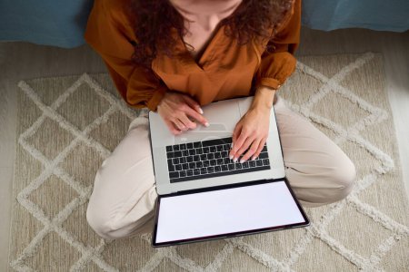 Foto de Above angle of young restful female with laptop sitting on gray rug on the floor by bed and shopping or communicating in the net - Imagen libre de derechos