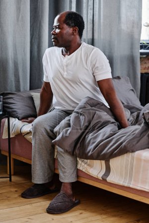 Foto de Hombre afroamericano mayor en pijama sentado en la cama por la mañana después de dormir bien y pensar en sus planes para el día - Imagen libre de derechos