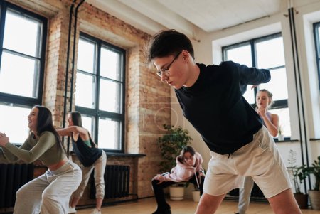 Téléchargez les photos : Male teenager in activewear bending forwards with his arms stretched behind back while training in dance hall with other teens - en image libre de droit