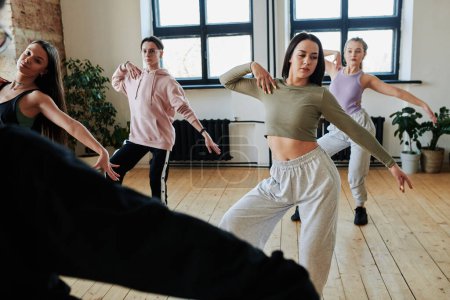 Téléchargez les photos : Teenage girls and guy in activewear repeating dancing exercise after their instructor or leader during training in spacious loft studio - en image libre de droit