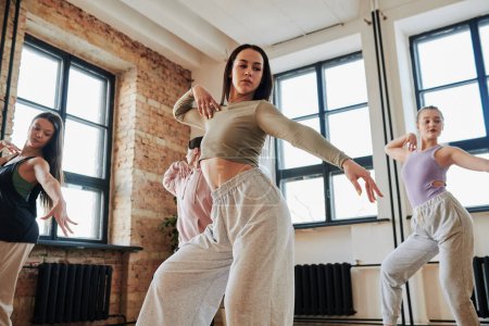 Téléchargez les photos : Groupe d'adolescents flexibles en vêtements de sport effectuant des mouvements de danse voge pendant l'entraînement dans un studio de loft moderne - en image libre de droit