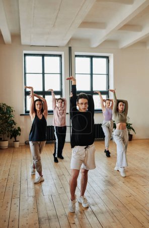 Téléchargez les photos : Young teenage male leader of performance group showing vogue dance exercises to group of girls and guy during training in studio - en image libre de droit