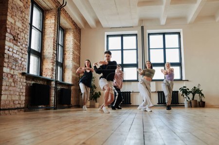 Foto de Group of energetic teenagers in activewear repeating vogue dance exercise after their leader of performance team in studio - Imagen libre de derechos
