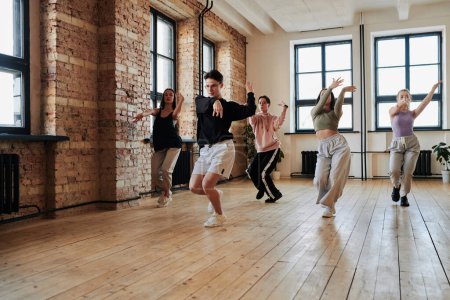 Téléchargez les photos : Leader of vogue dance performance group showing new movements to teenagers repeating after him during training in loft studio - en image libre de droit
