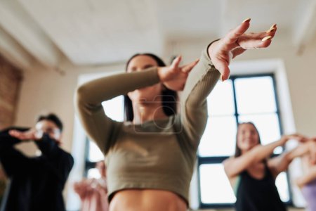 Foto de Hands of dynamic teenage girl stretching arms during vogue dance movement while showing it to group of youthful performers - Imagen libre de derechos