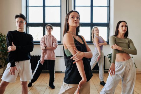 Téléchargez les photos : Group of contemporary teens in pants and tanktops repeating after dance instructor while learning new movements of vogue dancing - en image libre de droit