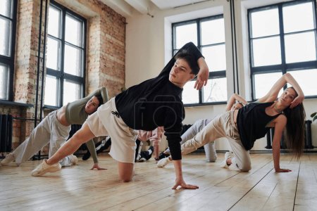 Photo for Instructor of vogue dance performance group showing new movements to teenagers in activewear during training in loft studio - Royalty Free Image