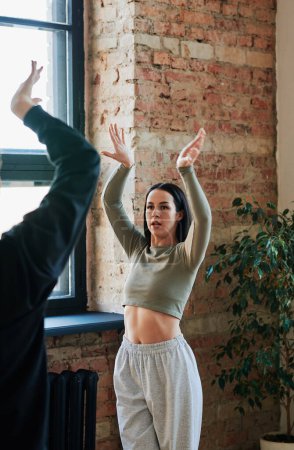 Téléchargez les photos : Young female instructor in activewear giving advice to male dancer during training while standing in front of him with raised arms - en image libre de droit