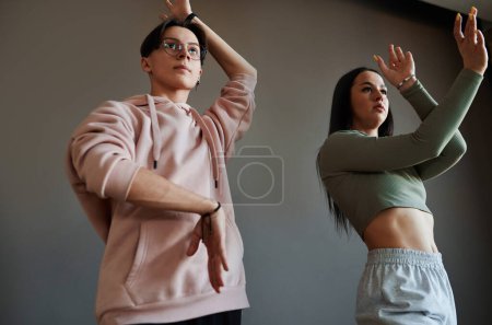 Téléchargez les photos : Adolescent actif contemporain et jeune fille aux bras levés dansant en vogue pendant la répétition contre un mur gris en studio - en image libre de droit