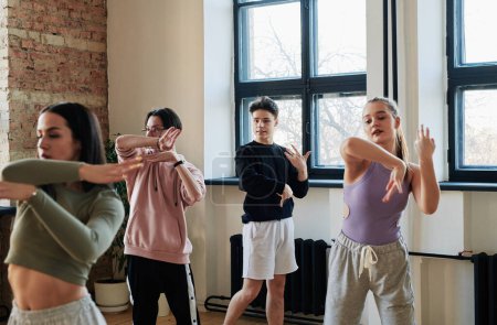 Téléchargez les photos : Young male instructor of vogue dancing group consulting teenage girls and guy in activewear repeating new movement at training - en image libre de droit