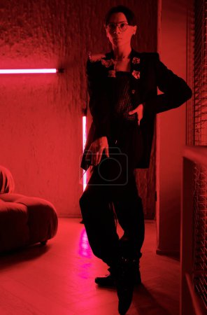 Photo for Posh young man in smart black attire performing vogue dance movements in red lit room of contemporary entertainment club - Royalty Free Image