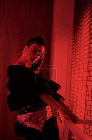 Téléchargez les photos : Jeune interprète contemporaine en tenue noire chic regardant la caméra tandis que la vogue danse en studio éclairée par la lumière rouge - en image libre de droit