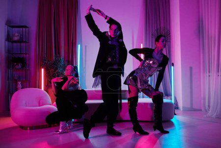 Téléchargez les photos : Small group of active teenage dancers in smart apparel taking part in vogue ball or performance in studio lit by neon lights - en image libre de droit