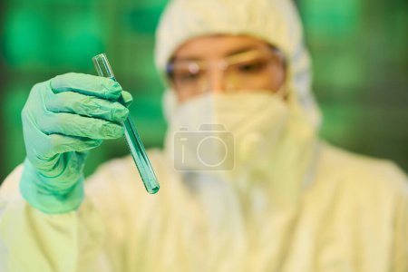 Téléchargez les photos : Main gantée d'un virologiste contemporain tenant une fiole contenant du liquide bleu tout en étudiant ses caractéristiques en laboratoire clinique - en image libre de droit