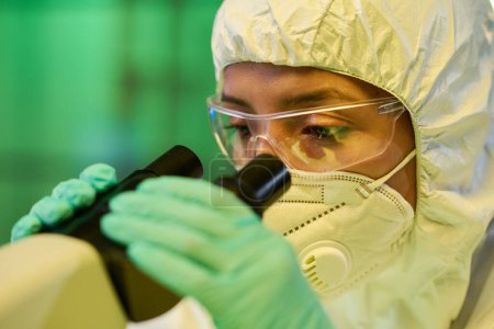 Téléchargez les photos : Virologiste féminine gantée en combinaison protectrice et lunettes étudiant les caractéristiques de la nouvelle souche de coronavirus en laboratoire clinique - en image libre de droit