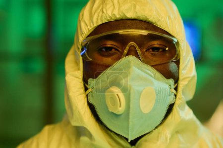 Téléchargez les photos : Visage de virologiste afro-américain en combinaison de protection, lunettes et respirateur debout devant la caméra en laboratoire - en image libre de droit