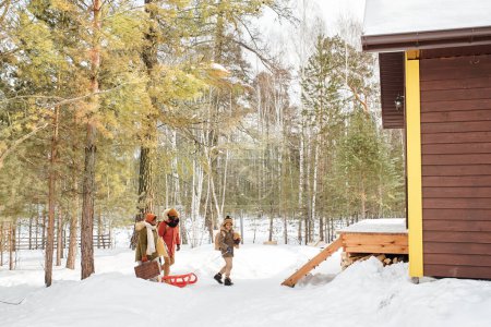 Foto de Contemporary black family of three in winterwear moving towards their country house located in the forest to spend weekend there - Imagen libre de derechos