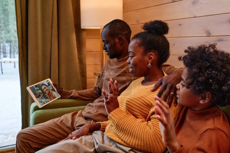 Téléchargez les photos : Contemporary African American family greeting their friends on tablet screen during online communication in their country house - en image libre de droit
