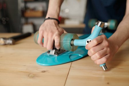 Photo for Hands of contemporary teenager repairing his skateboard in house garage while fixing wheels on back side of board of blue color - Royalty Free Image