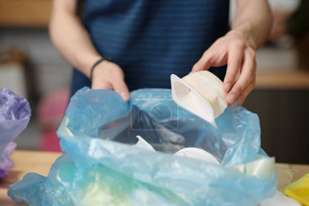 Foto de Hands of youthful guy putting white small plastic food container into cellophane sack while sorting various types of waste - Imagen libre de derechos