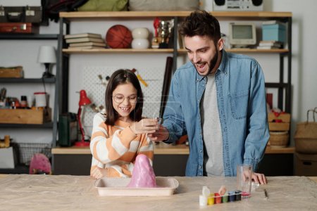 Photo for Cute little girl and her father looking at chemical reaction in handmade volcano after mixing several ingredients to imitate eruption - Royalty Free Image