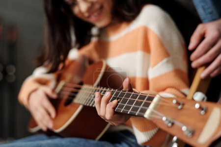 Photo for Hand of contemporary little girl learning to play guitar at leisure while keeping finger on one of strings during lesson with tutor - Royalty Free Image