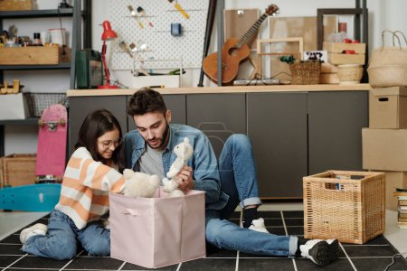 Photo for Cute little girl and her father in casualwear sitting on the floor of garage and taking toys out of boxes while playing together at leisure - Royalty Free Image