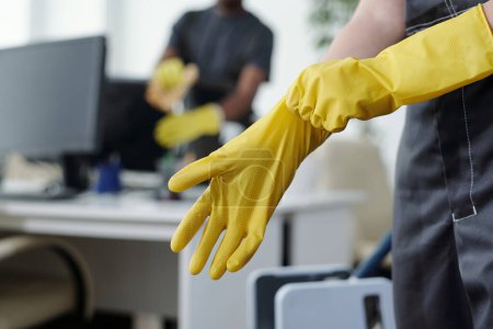 Photo for Hands of female worker of contemporary cleaning company putting on yellow protective rubber gloves before mopping floor of office - Royalty Free Image