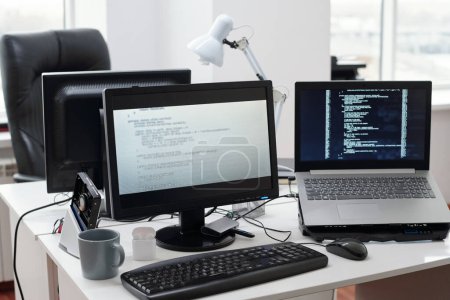 Téléchargez les photos : Données décodées sur les écrans d'ordinateur et d'ordinateur portable debout sur le lieu de travail du programmeur contemporain dans un grand bureau ouvert - en image libre de droit