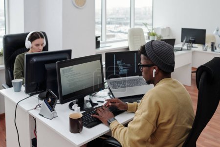 Téléchargez les photos : Programmeurs interculturels contemporains assis devant des ordinateurs dans un grand bureau ouvert et travaillant sur de nouveaux logiciels - en image libre de droit