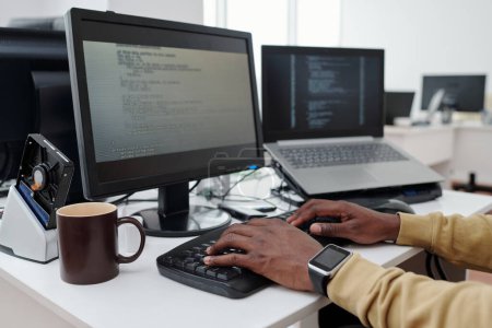 Téléchargez les photos : Mains de jeune programmeur masculin ou it-ingénieur décodage des données sur l'écran de l'ordinateur tout en appuyant sur les boutons du clavier dans le bureau - en image libre de droit