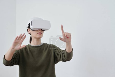Photo for Young contemporary female employee in vr headset pointing at object in virtual reality while making presentation of new project - Royalty Free Image