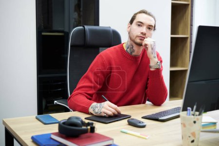 Photo for Portrait of young graphic designer looking at camera while sitting at table with computer and working on graphic tablet - Royalty Free Image