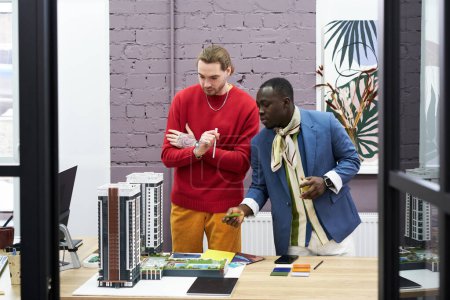 Téléchargez les photos : Designer africain veste de mode discutant du projet de maquettes de bâtiments avec son collègue au bureau - en image libre de droit