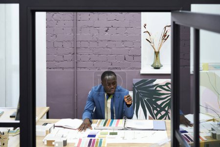 Foto de Diseñador africano masculino que trabaja con paleta de colores en la mesa de la oficina moderna - Imagen libre de derechos