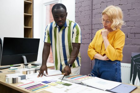 Foto de Dos diseñadores eligen el color en la paleta en la mesa y discuten el nuevo interior durante el trabajo en equipo en la reunión - Imagen libre de derechos