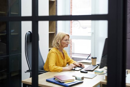 Téléchargez les photos : Femme graphiste mature se concentrant sur son travail sur ordinateur avec tablette graphique à l'étude au bureau - en image libre de droit