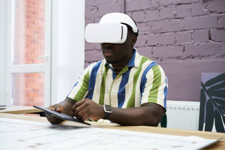 Foto de African young designer working in virtual reality headset at his workplace at office - Imagen libre de derechos