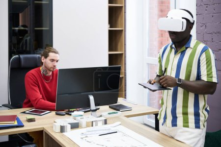 Foto de Diseñador gráfico usando auriculares VR para dibujar planos con tableta con su colega usando el ordenador en la mesa - Imagen libre de derechos