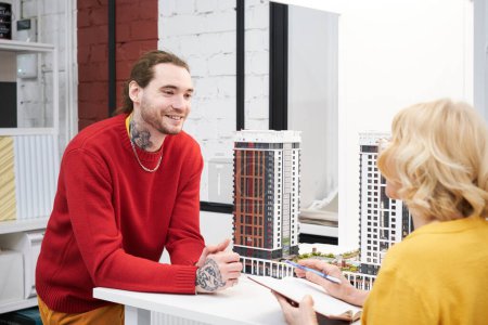 Téléchargez les photos : Jeune architecte souriant lors d'une conversation avec une femme d'affaires, ils discutent du projet de construction de nouveaux gratte-ciel - en image libre de droit