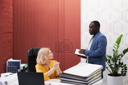 Foto de Hombre de negocios africano hablando con el gerente y tomando notas en el cuaderno durante su conversación en la oficina - Imagen libre de derechos