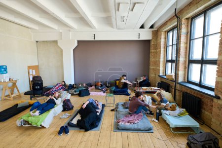 Foto de Varios lugares para dormir con personas sin hogar temporalmente descansando y comunicándose entre sí en una habitación espaciosa - Imagen libre de derechos