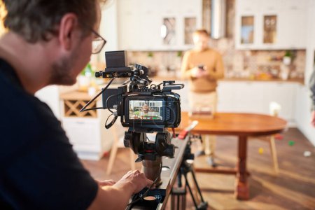 Photo for Young male videographer standing by video camera while shooting advertisement of cooking or masterclass in the kitchen - Royalty Free Image