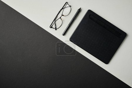 Foto de Plancha de tableta de diseñador gráfico, lápiz óptico y anteojos en escritorio gris con parte negra y espacio de copia para su texto o anuncio - Imagen libre de derechos