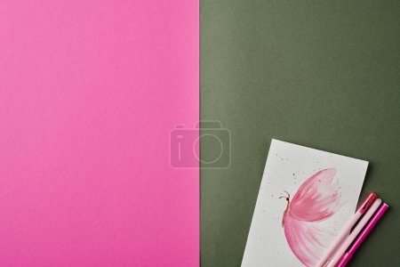 Photo for Flatlay of pink poster, paper with watercolor drawing of butterfly and group of highlighter and pens over gray background - Royalty Free Image