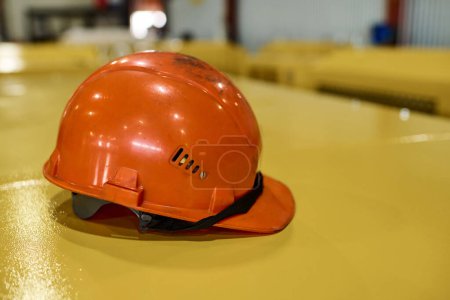 Foto de Protective helmet of orange color on yellow metallic cover of industrial machine or other equipment inside workshop of modern factory - Imagen libre de derechos