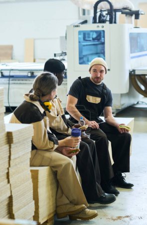 Téléchargez les photos : Group of workers in uniform drinking coffee and talking to each other while resting after work in warehouse - en image libre de droit